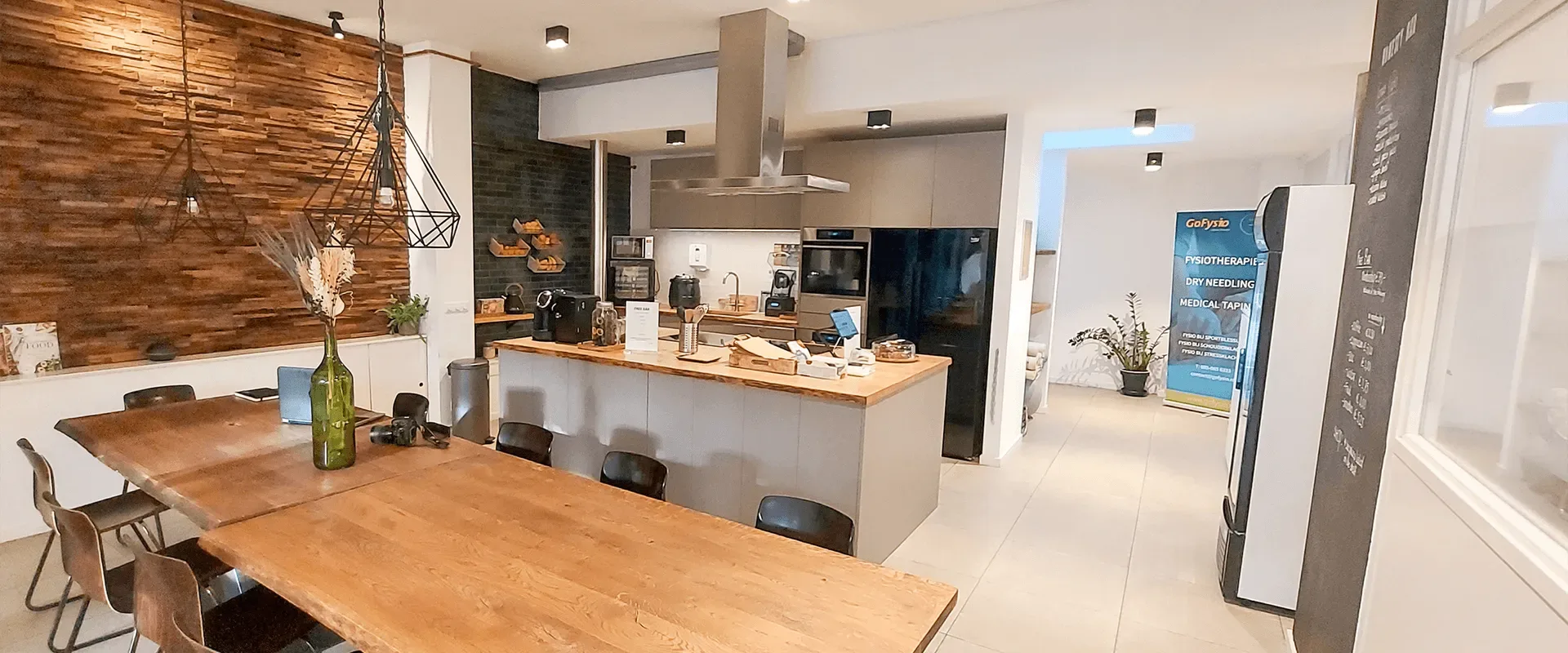 De open keuken en lange tafel van BeyondFit, met houten wand en hanglampen