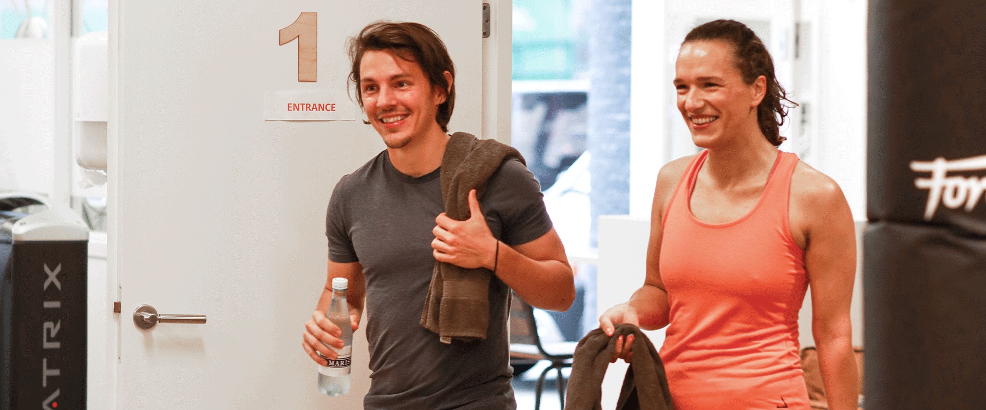 Twee leden komen na hun training lachend door de entree van BeyondFit